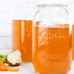 three jars of vegetable broth with vegetable scraps on lower left side.