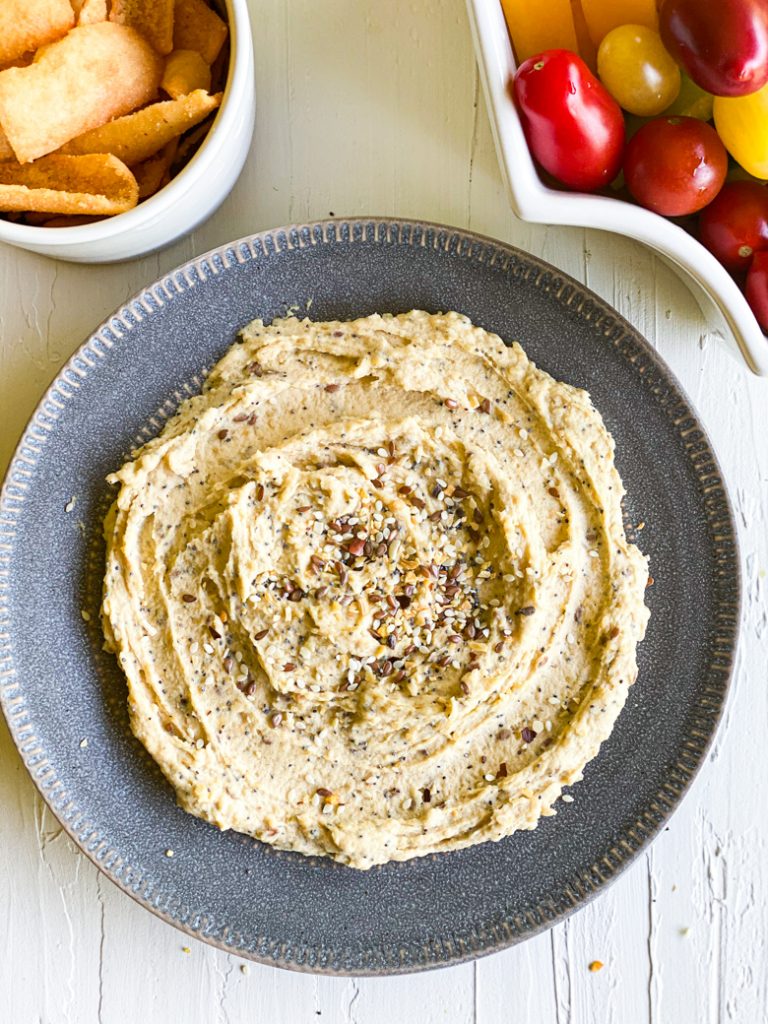 Everything bagel hummus on a plate. Upper right bowl of pita upper left cherry tomatoes. 