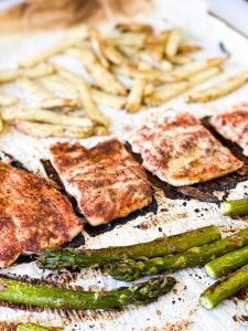 baked maple cajun salmon with potatoes and asparagus on parchment paper covered sheet pan